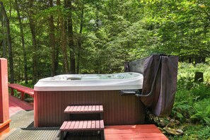 Ein Whirlpool inmitten eines bewaldeten Geländes mit einer Holzterrasse und Stufen, die hinauf führen.