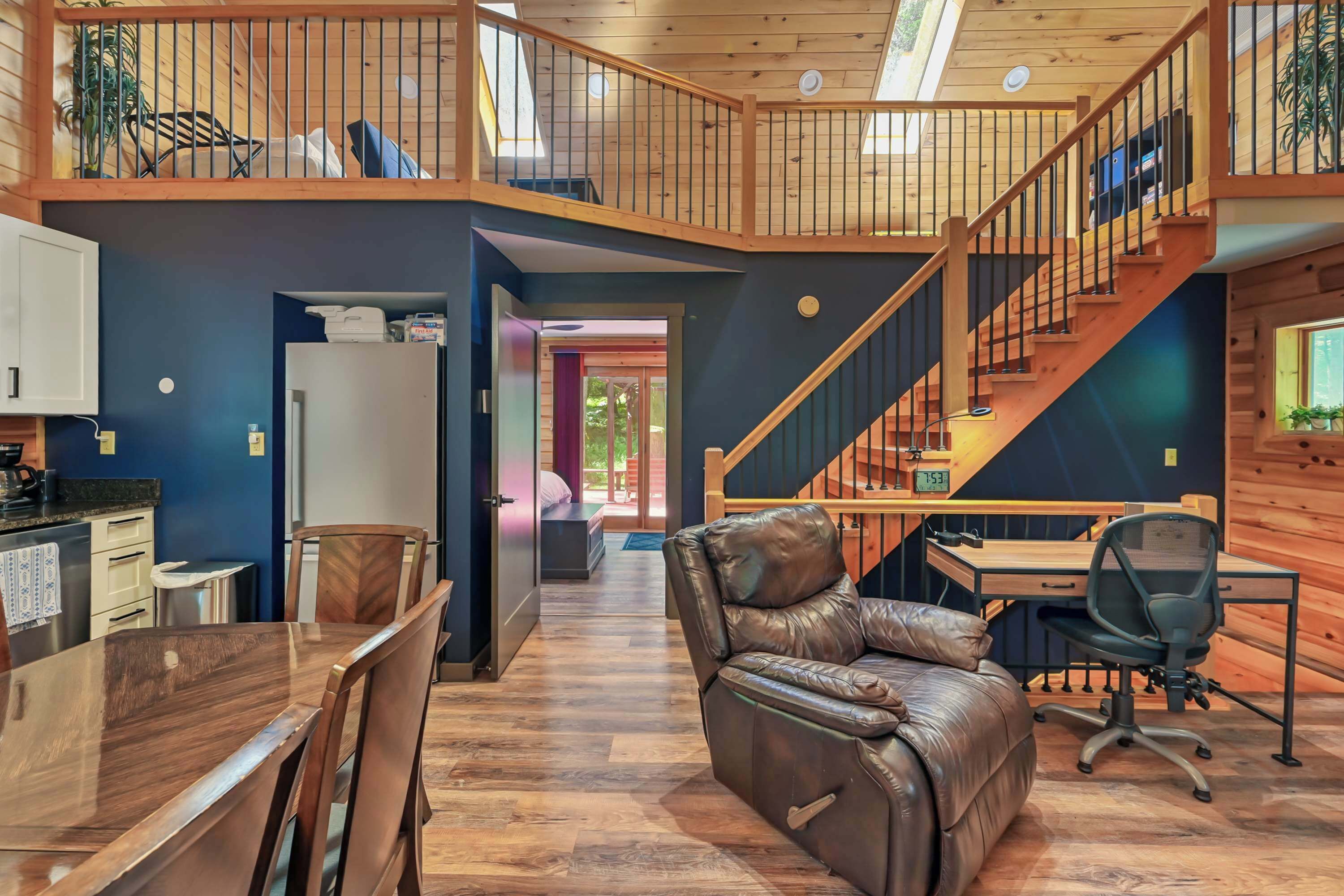 A spacious loft with a dining area, a leather chair, a desk with a computer, and a staircase.