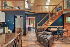 Ein geräumiges Loft mit Essbereich, einem Ledersessel, einem Schreibtisch mit Computer und einer Treppe.