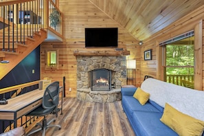 Ein Ferienhaus-Interieur mit Kamin aus Stein, einer blauen Couch, einem Holztisch und einer Treppe.