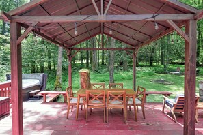 A covered outdoor dining area with a wooden table and chairs, surrounded by a deck with a red railing. - Contemporary 2BR Cabin - HOT TUB & Fireplace - Oakland (Oakland)