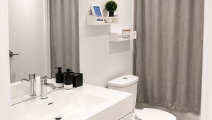 Ett modernt badrum med ett vitt handfat, en stor spegel, en toalett och ett duschdraperi.