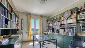 Et bibliotek med bogreoler, et glasbord og udsigt gennem et vindue.