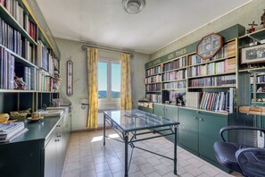 Eine Bibliothek mit Bücherregalen, einem Glastisch und Blick durch ein Fenster.