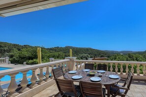 Eine Terrasse mit Esstisch, ein Schwimmbad und Blick auf grüne Hügel.