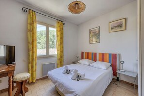 Ein Hotelzimmer mit Bett, Schreibtisch, Fernseher und einem fenster mit Vorhängen.