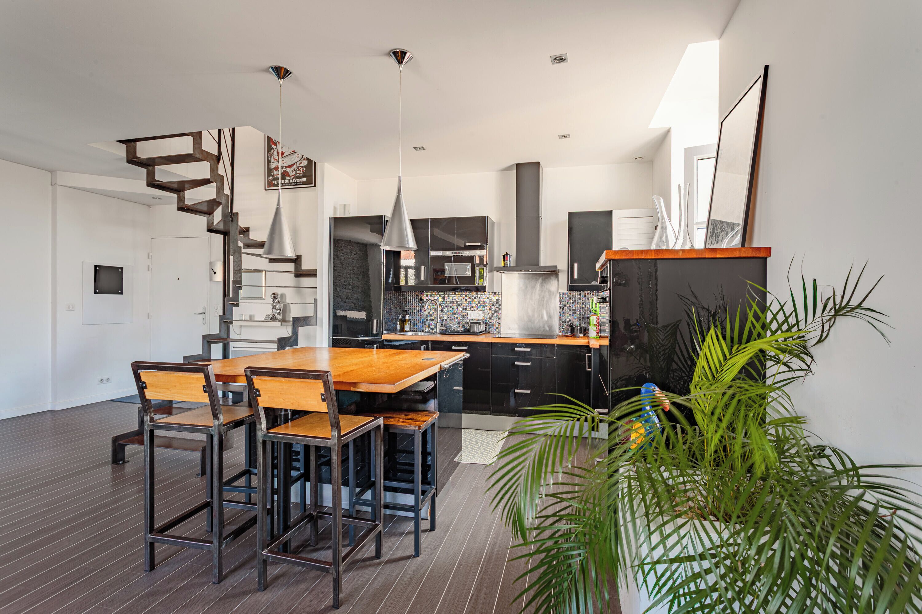 Eine moderne Küche mit einem Holzespeisetisch und Stühlen, einer Treppe und einem Blumentopf.
