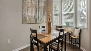 Un comedor con una mesa de madera, cuatro sillas, un florero y un cuadro abstracto grande en la pared.