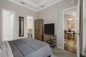 A bedroom with a bed, a wardrobe, a TV on a stand, and a dining area visible through an open door. - Home on Hays ~10 from FSU and FAMU (Tallahassee)
