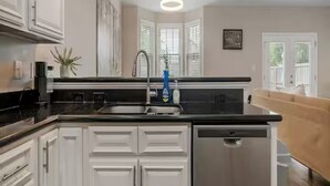 Una cocina con muebles blancos, lavavajillas de acero inoxidable y encimera negra.