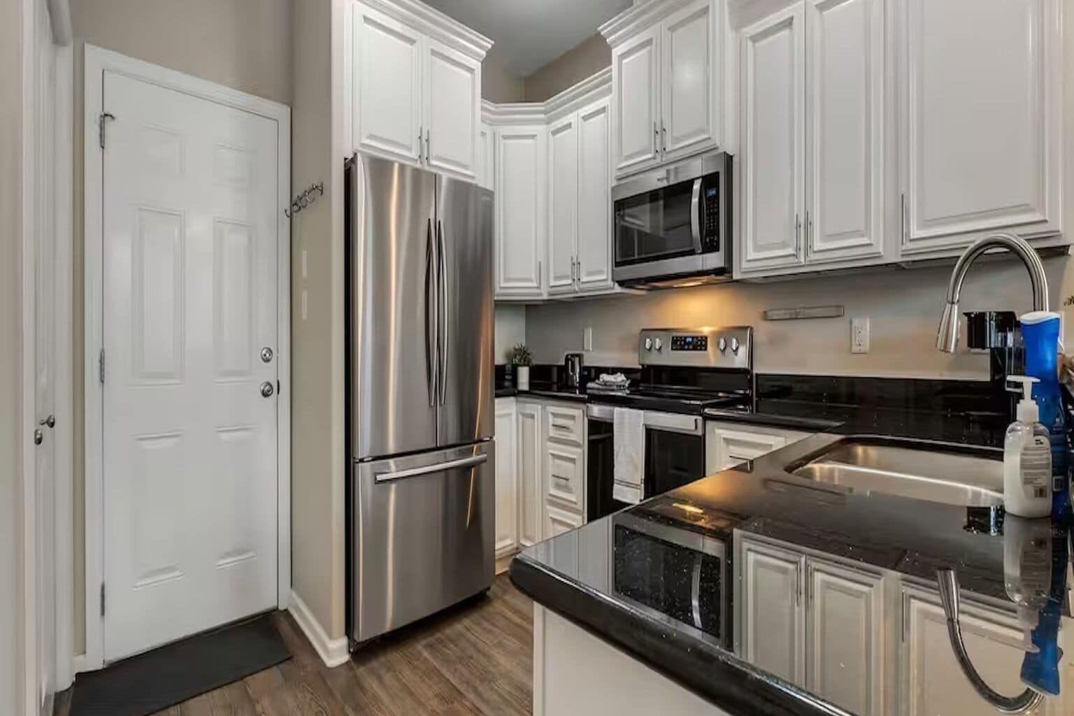 A kitchen with white cabinets, stainless steel appliances, a black countertop, and a stainless steel sink.