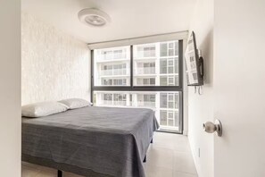 Een slaapkamer met een bed, een raam en een deur met een lichtschakelaar.