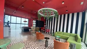 A modern lounge area with a patterned floor, green sofa, orange armchairs, and a unique circular light fixture. - 906 Sky Garden (San José)