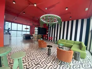 Eine moderne Lounge mit einem gemusterten Boden, einer grünen Couch, orangefarbenen Sessel und einer außergewöhnlichen, runden Leuchte.