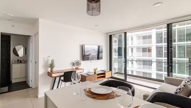 A modern living room with a dining area, a kitchen, and a large window with a view of a building. - 906 Sky Garden (San José)