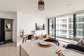 A modern living room with a dining area, a kitchen, and a large window with a view of a building. - 906 Sky Garden (San José)