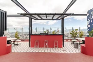 Een dakterras met helder uitzicht op de stadszicht, met een bar, krukken en terrasstoelen.