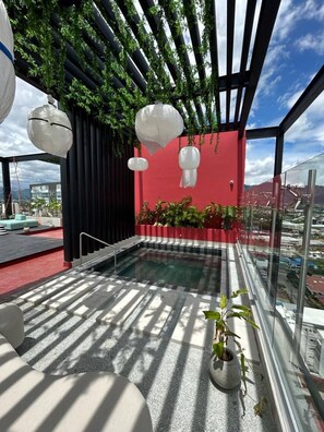 Une piscine sur le toit, avec un mur rouge, des lanternes suspendues et une vue sur le paysage urbain.