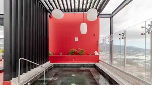 A rooftop pool with a red wall, a glass railing, and a view of the city. - 906 Sky Garden (San José)