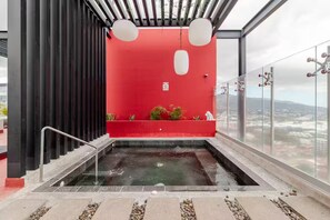 Ein Pool auf dem Dach mit einer roten Wand, einem Glasgeländer und Blick auf die Stadt.