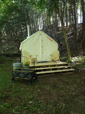 A tent with a ramp, two chairs, a trash bin, and a cart in a forest.
