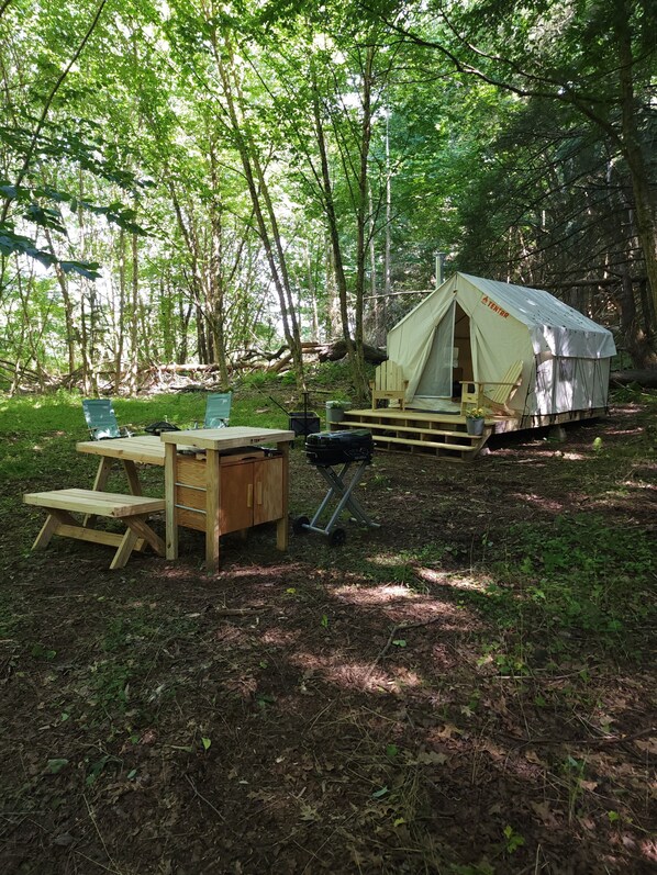 A tented camping area with a table and chairs, surrounded by trees.