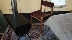 Ein Zeltinnenraum mit einem Bett, einem Stuhl, einem Herd und einem Fenster.