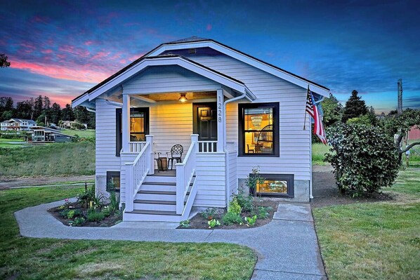 A single-story house with a front porch, a small garden, and an American flag.