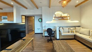 A modern living room with a flat-screen TV, a wooden dining table, a sofa, and a hanging light fixture.