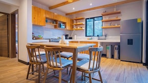 A modern kitchen with wooden cabinets, a central island with chairs, a stainless steel refrigerator, and a window providing natural light.