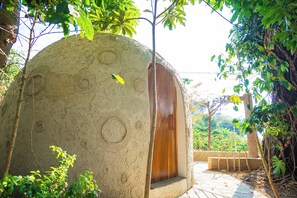 Una estructura abovedada con puerta de madera, rodeada de follaje y un sendero de piedra.