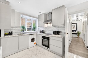 A modern kitchen with white cabinetry, a built-in washing machine, and a stove. - Family-friendly 2-bed apartment near station, sleeps 5 (London)