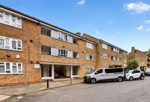 A multi-story residential building with a brick facade, a covered entrance, and a parking area with cars. - Family-friendly 2-bed apartment near station, sleeps 5 (London)