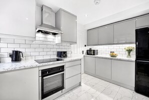 A modern kitchen with white cabinetry, a black stove, and a microwave. - Family-friendly 2-bed apartment near station, sleeps 5 (London)