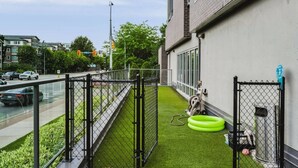 A fenced outdoor area with artificial grass, a green tire swing, and a metal gate. - The Knox | Central Pet-Friendly Kelowna 2BR Condo (Kelowna)