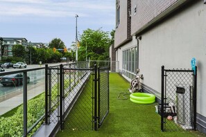 A fenced outdoor area with artificial grass, a green tire swing, and a metal gate. - The Knox | Central Pet-Friendly Kelowna 2BR Condo (Kelowna)