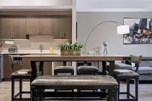 A modern kitchen with a central island, built-in cabinets, and a dining area with a bench and chairs. - The Knox | Central Pet-Friendly Kelowna 2BR Condo (Kelowna)