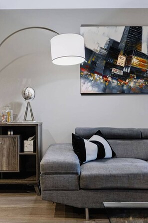 Ein modernes Wohnzimmer mit einem grauen Sofa, einer Lampe, einer Anrichte und einem Stadtbild an der Wand.