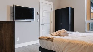 A bedroom with a bed, a television mounted on the wall, a wardrobe, and a window. - The Knox | Central Pet-Friendly Kelowna 2BR Condo (Kelowna)
