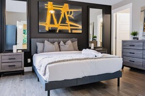 Ein modernes Schlafzimmer mit einem großen Bett, einem dunklen Kopfteil und einem großen abstrakten Gemälde darüber.