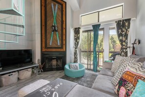 A living room with a fireplace, a sofa, a television, and a large window with curtains. - Walk to Town/ Golf; Pool and Hot Tub (Park City)