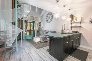 A modern kitchen with a central island, a staircase with a mesh railing, and a large wall clock. - Walk to Town/ Golf; Pool and Hot Tub (Park City)