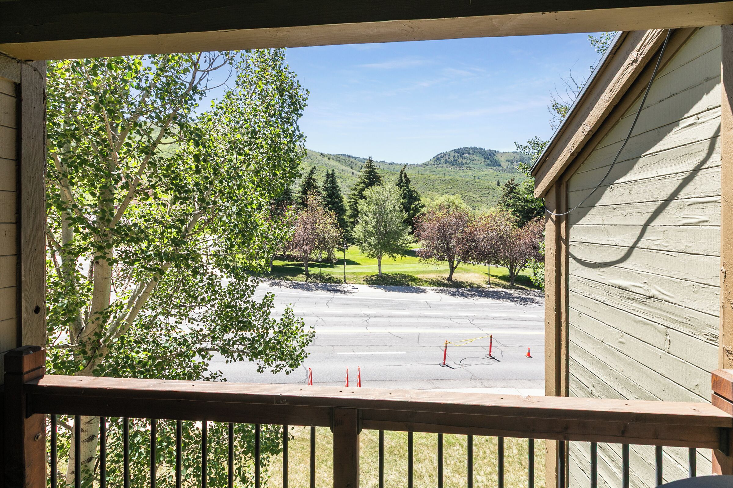 A view from a wooden balcony overlooking a parking area with trees and a hilly landscape.