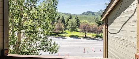 A view from a wooden balcony overlooking a parking area with trees and a hilly landscape.