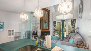 Eine Küche mit einer grünen Arbeitsplatte, einem Spülbecken und einer Wendeltreppe. Es gibt einen Wohnbereich mit einer Couch und einem Kamin.