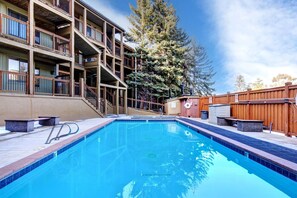 A swimming pool with a wooden deck, a wooden fence, and a multi-story building with balconies. - Walk to Town/ Golf; Pool and Hot Tub (Park City)