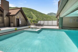 A swimming pool with a view of a mountain, a covered area with tables, and a building with a sign. - True Ski In/ Out 3 BD Lodge at Mtn Village, Pool, Hot Tub, Fitness (Park City)