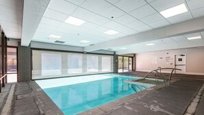 Ein Schwimmbecken mit klarem Wasser, umgeben von einem gefliesten Boden und Wänden mit Fenstern.