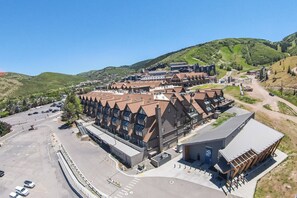 A modern hotel with a central courtyard, multiple floors, and a mountain backdrop. - True Ski In/ Out 3 BD Lodge at Mtn Village, Pool, Hot Tub, Fitness (Park City)