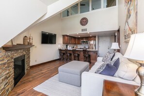 A spacious living area with a fireplace, a sofa, a kitchen in the background, and a high ceiling. - True Ski In/ Out 3 BD Lodge at Mtn Village, Pool, Hot Tub, Fitness (Park City)